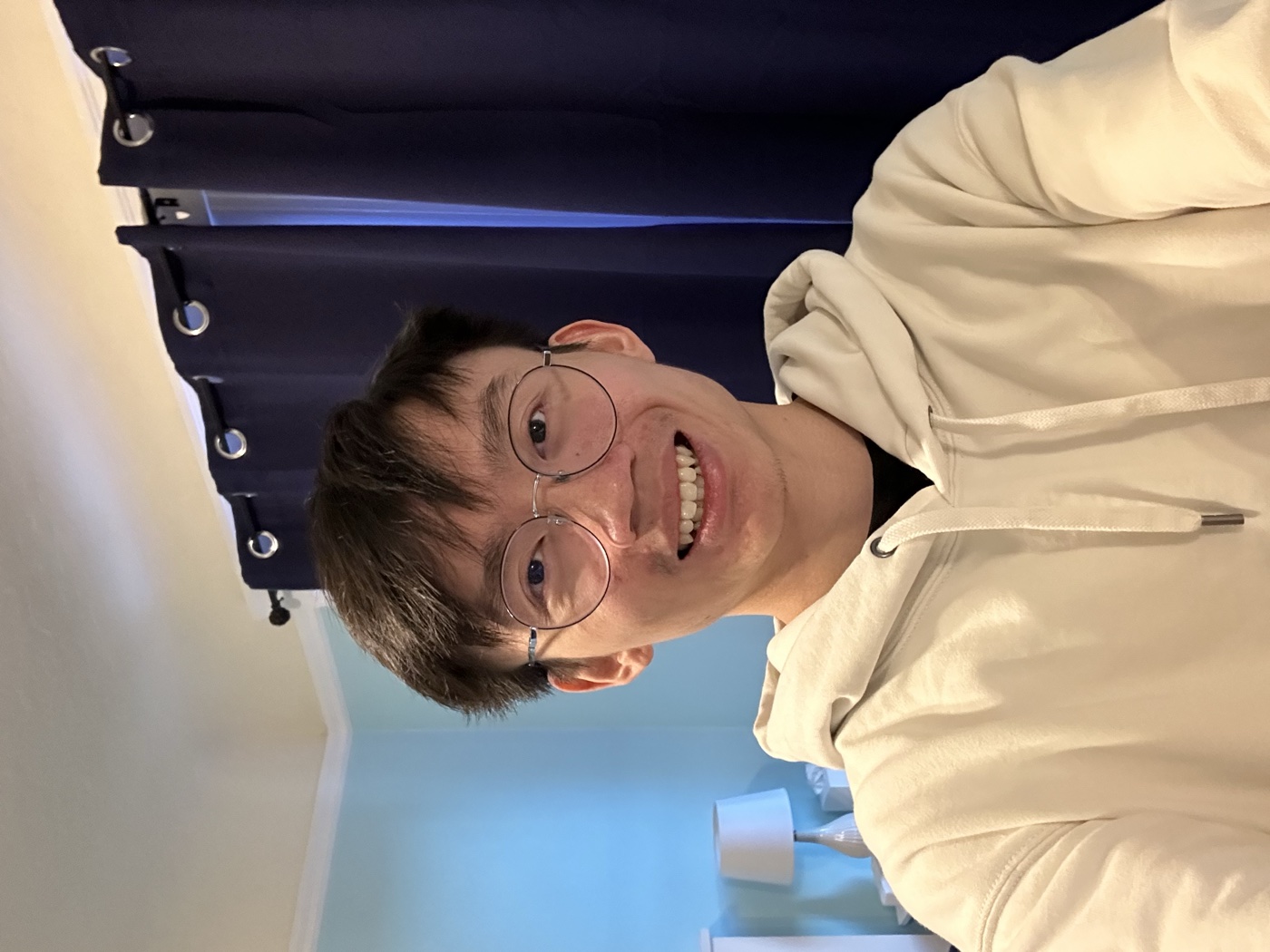 Jack Min Ong smiling, wearing glasses and a cream hoodie